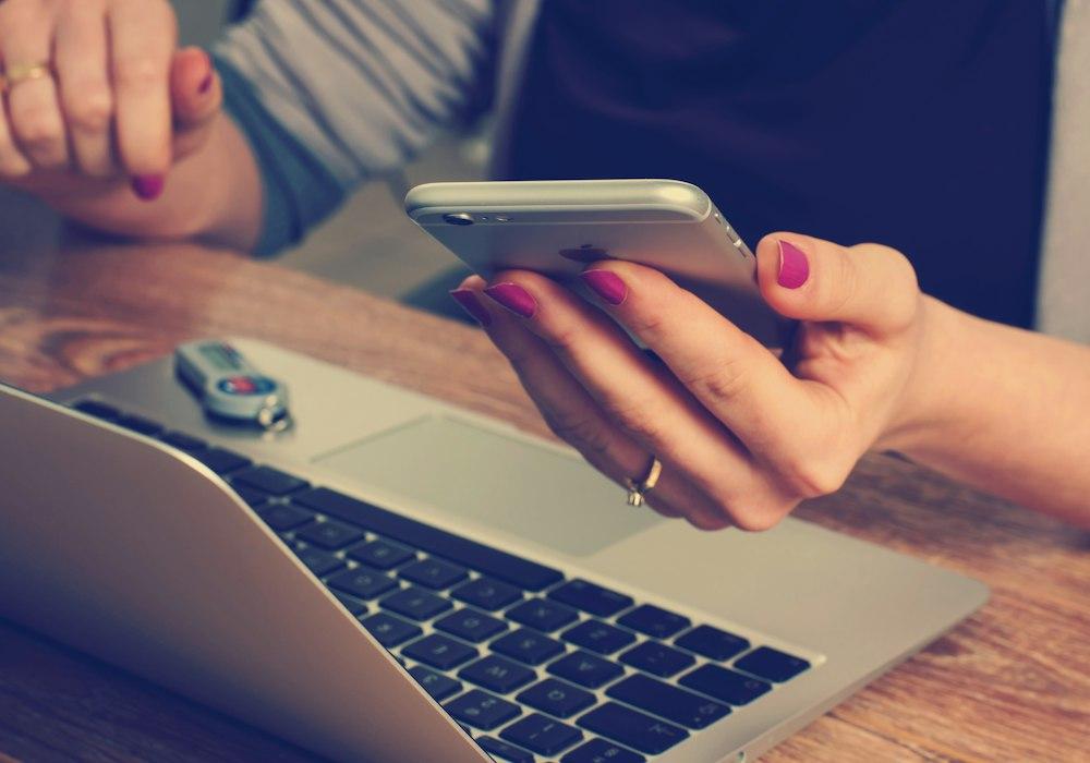 A person using a phone and laptop at a desk